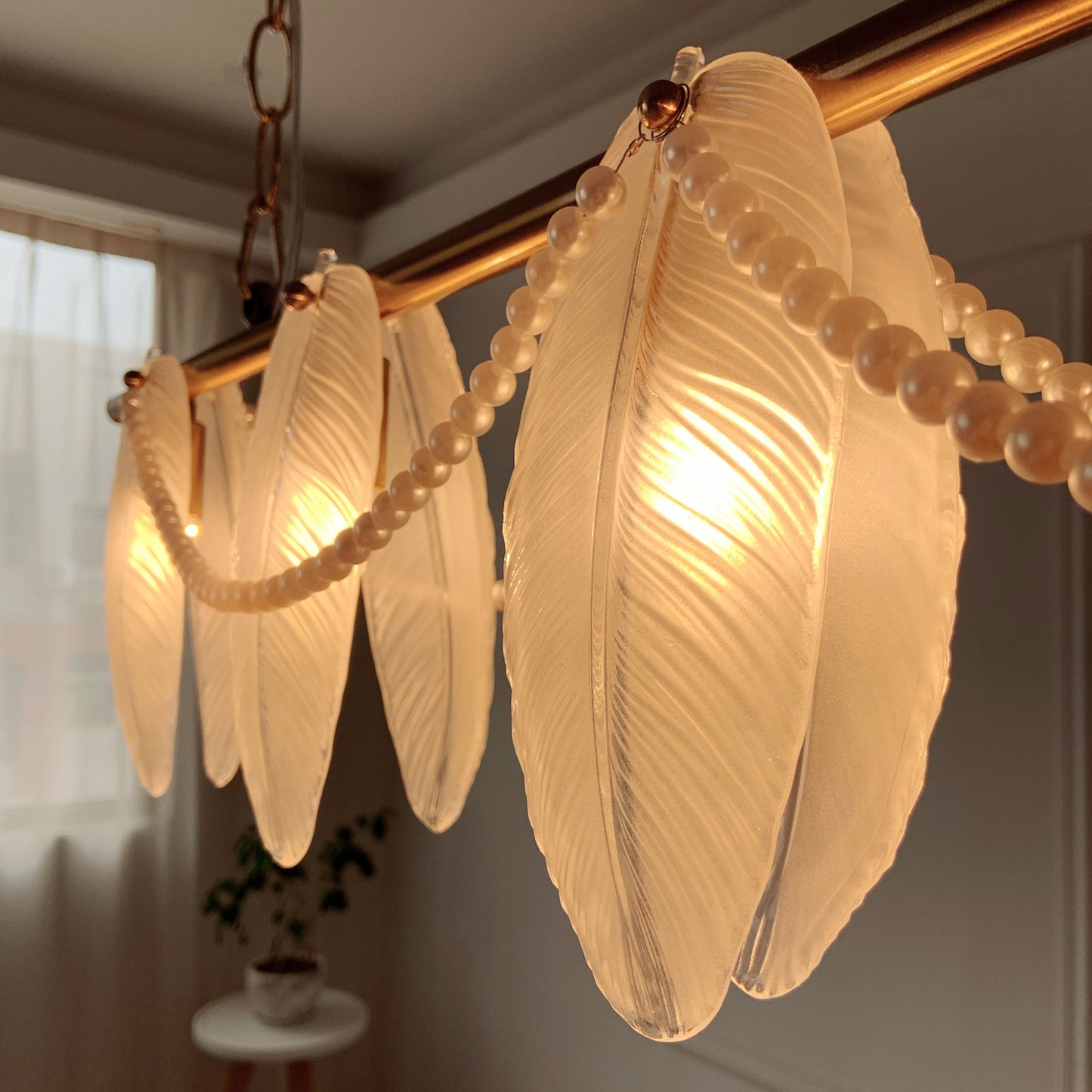 Chandelier with leaf-shaped glass shades and pearl-like beads in a softly lit room.