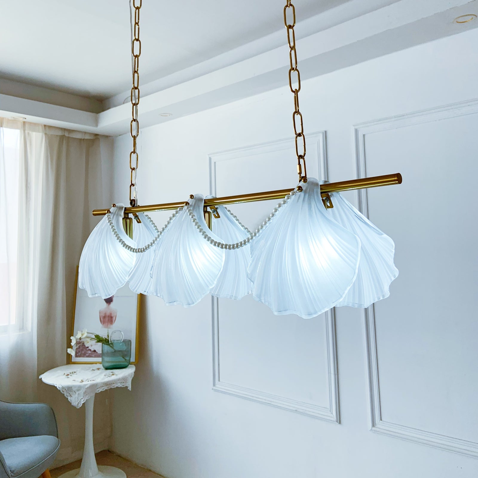 Chandelier with scallop shell design in a room with white walls and a curtain.