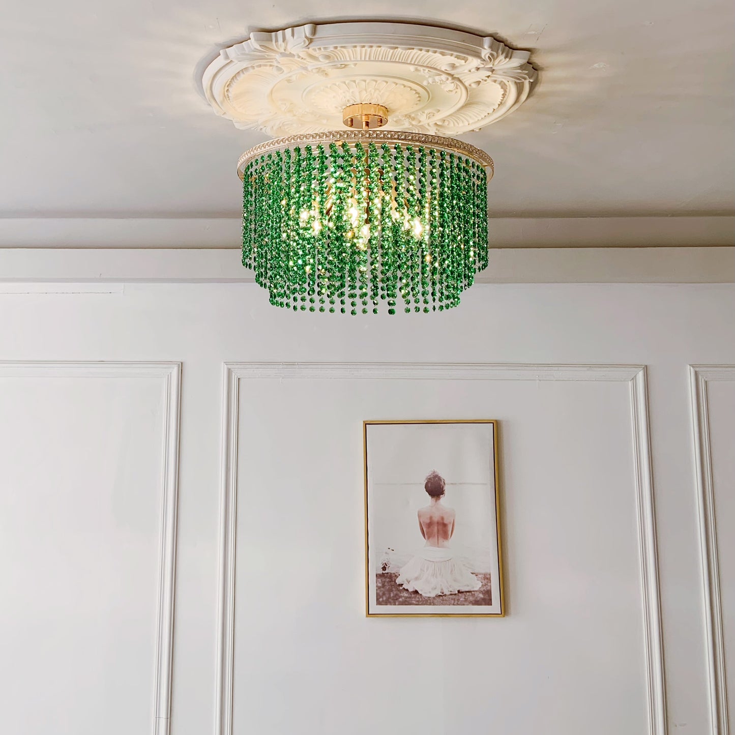 Green beaded chandelier hanging in a room with white walls and a framed picture.