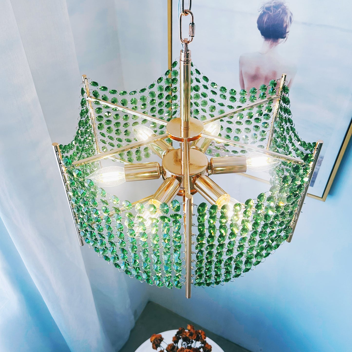 Gold chandelier with green crystals in a room with light blue walls and a white curtain.