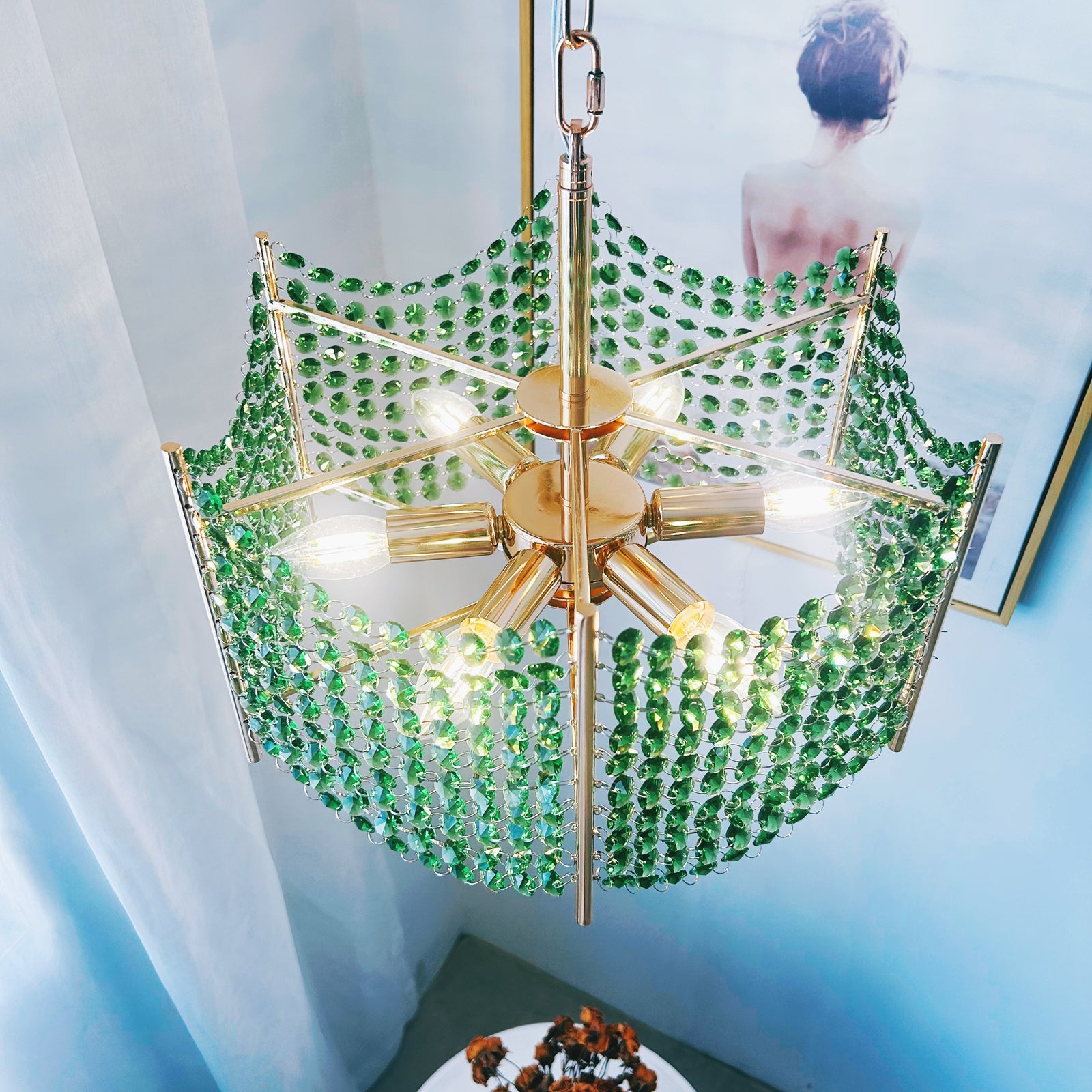 Gold chandelier with green crystals in a room with light blue walls and a white curtain.