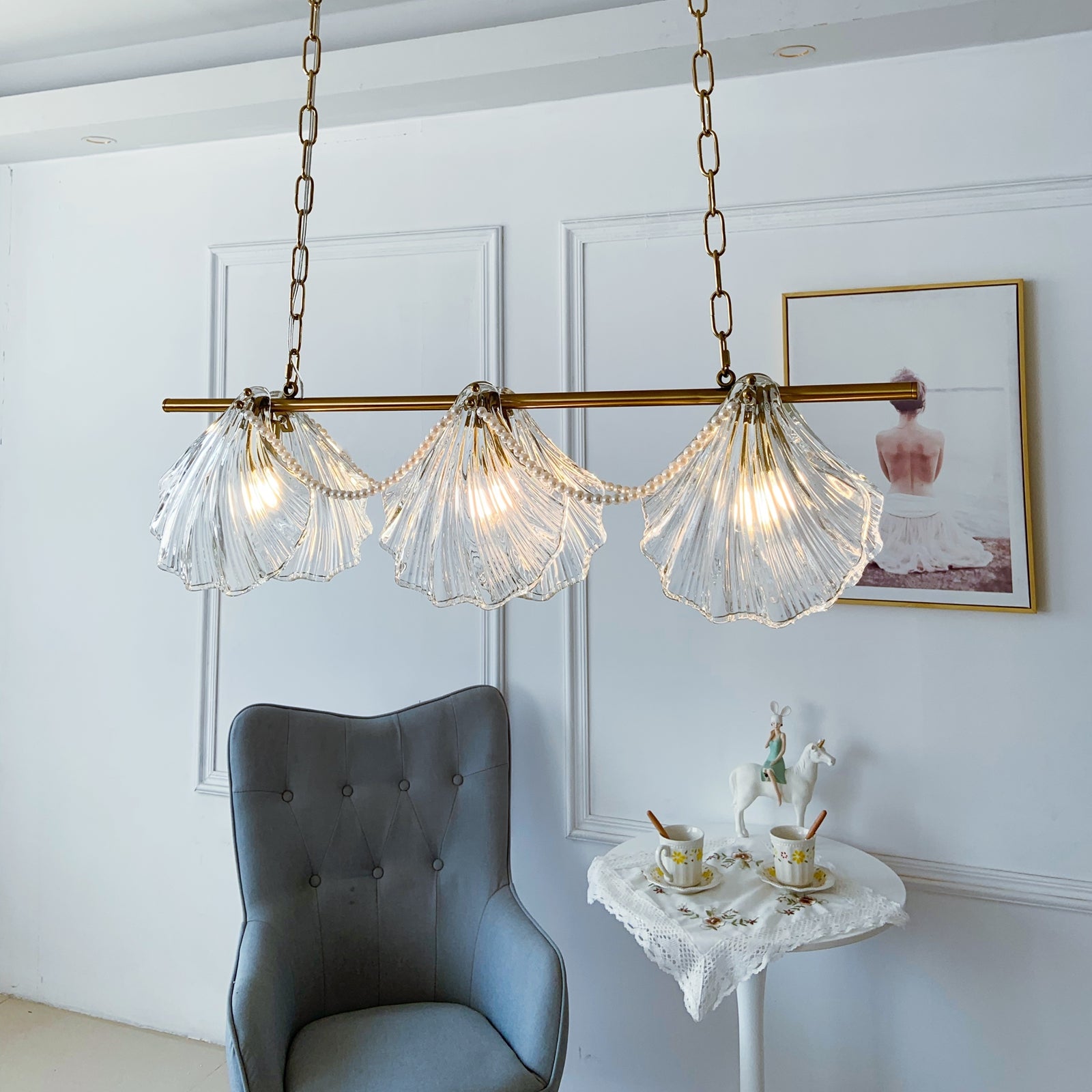 Modern chandelier with glass shades in a room with a gray chair and decorative items.