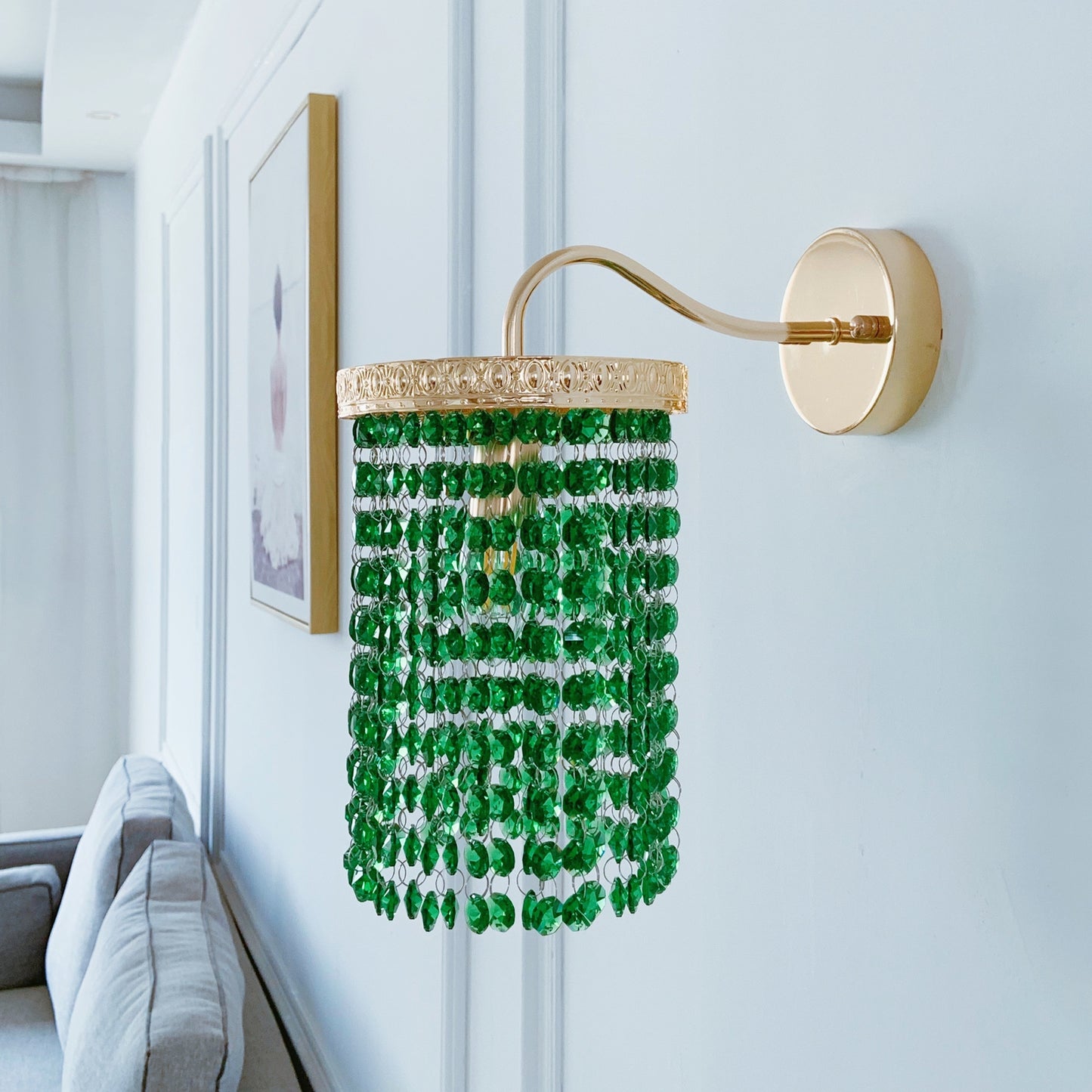 Decorative wall light fixture with green beads and gold accents on a white wall.