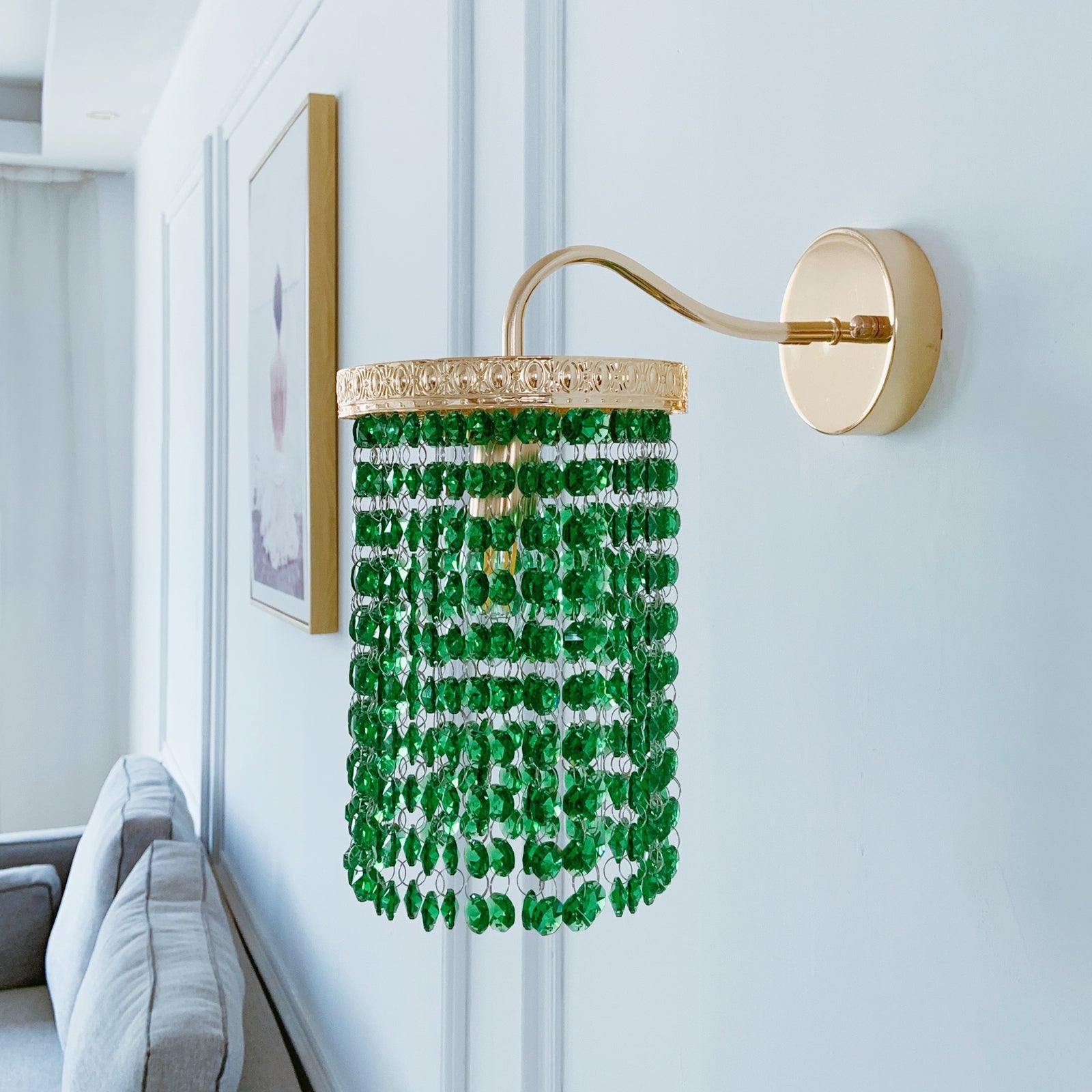 Decorative wall light fixture with green beads and gold accents on a white wall.