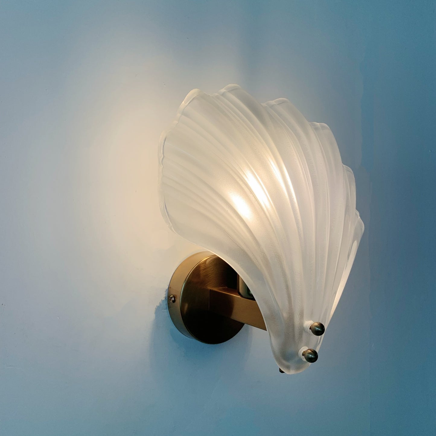 Wall-mounted light fixture with a white glass shade and gold metal base