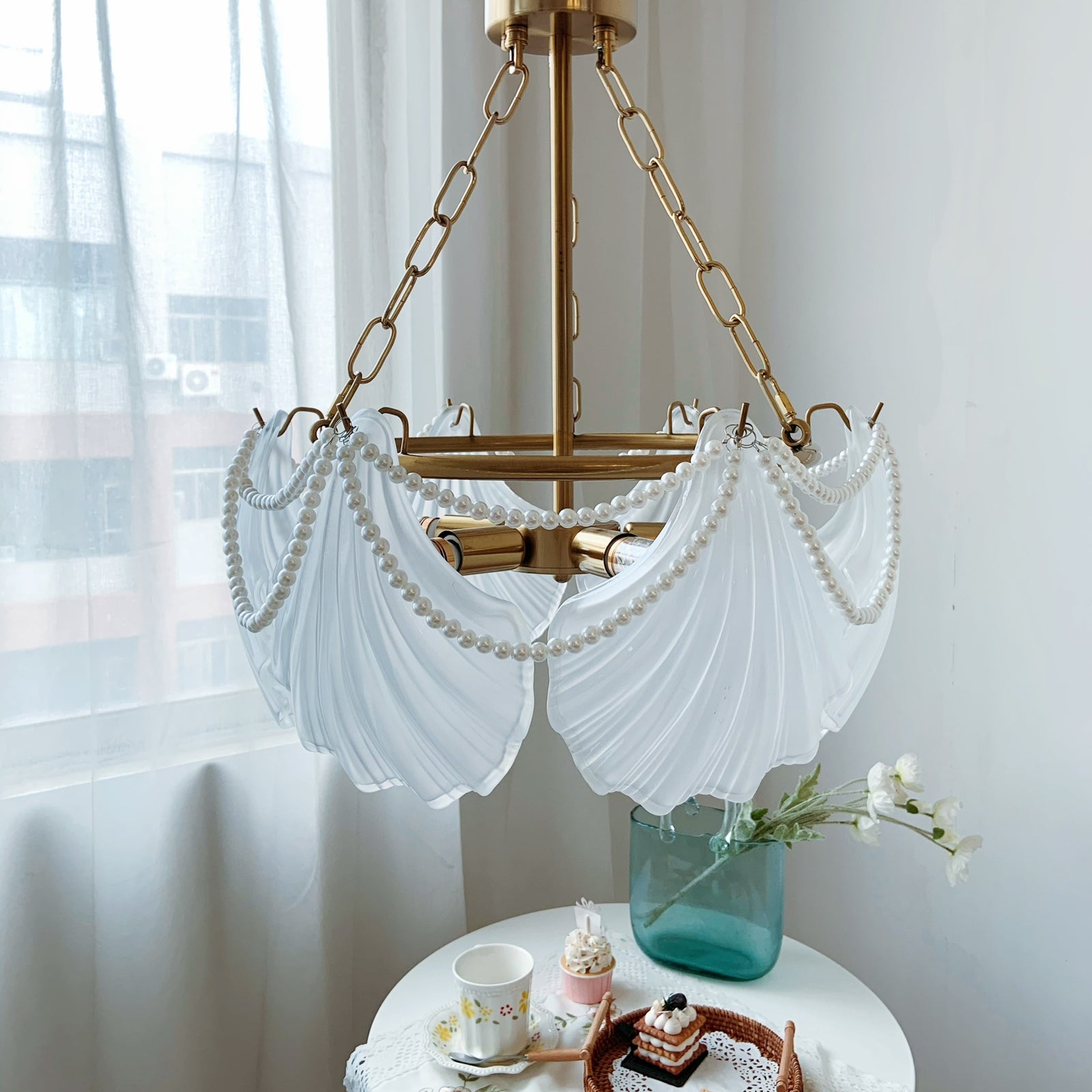 Decorative chandelier with white fabric shades in a room with light curtains.