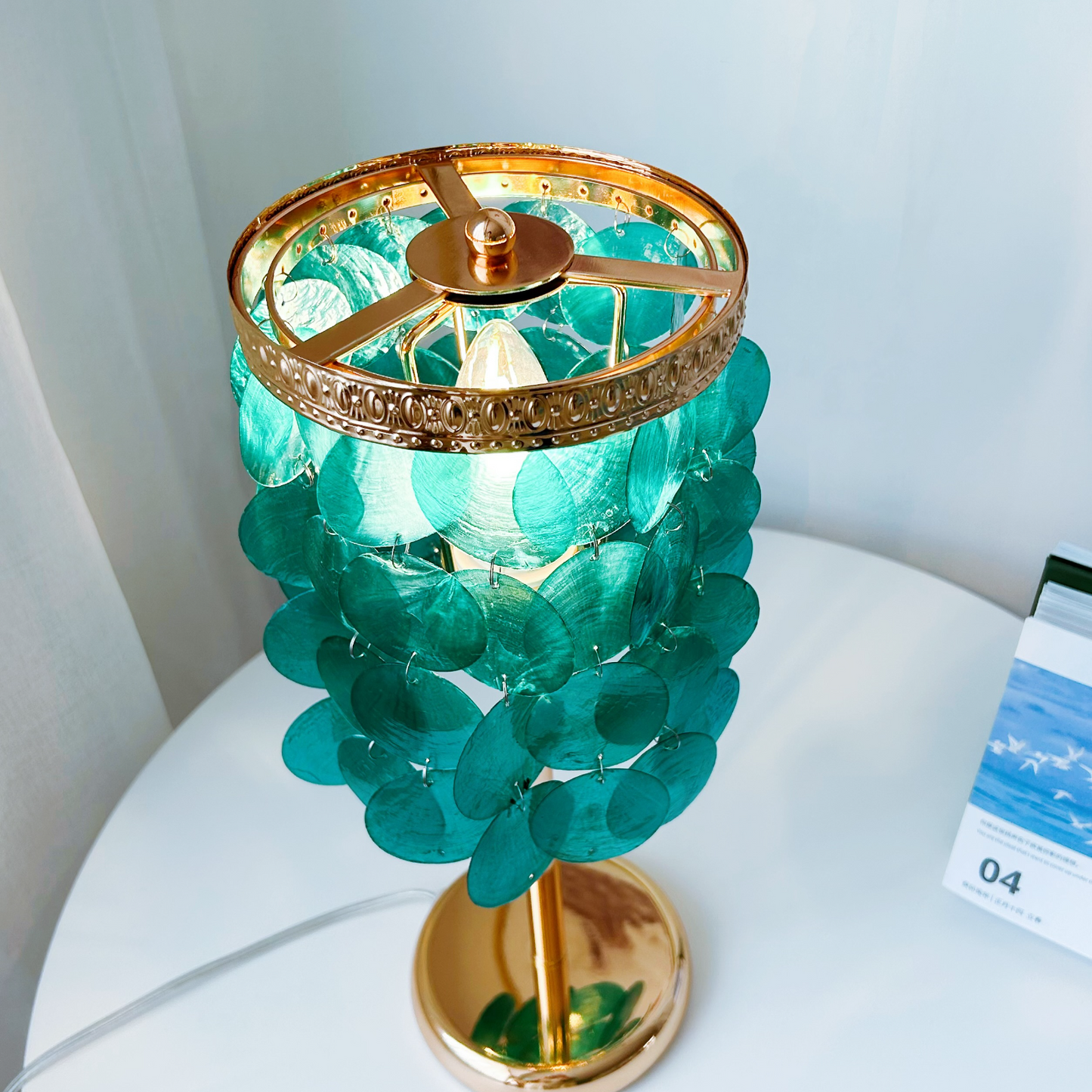 Handcrafted capiz shell lamp with ocean blue shells creating warm ambient lighting on nightstand