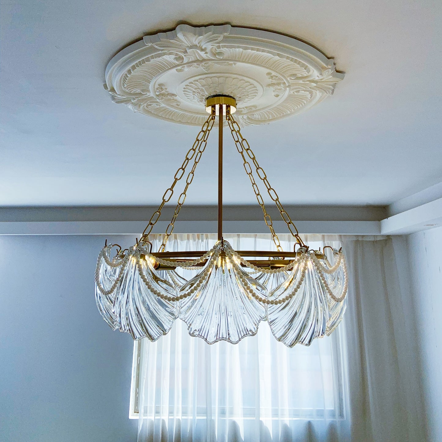 Decorative chandelier with clear glass and gold chains hanging from a ornate ceiling medallion.