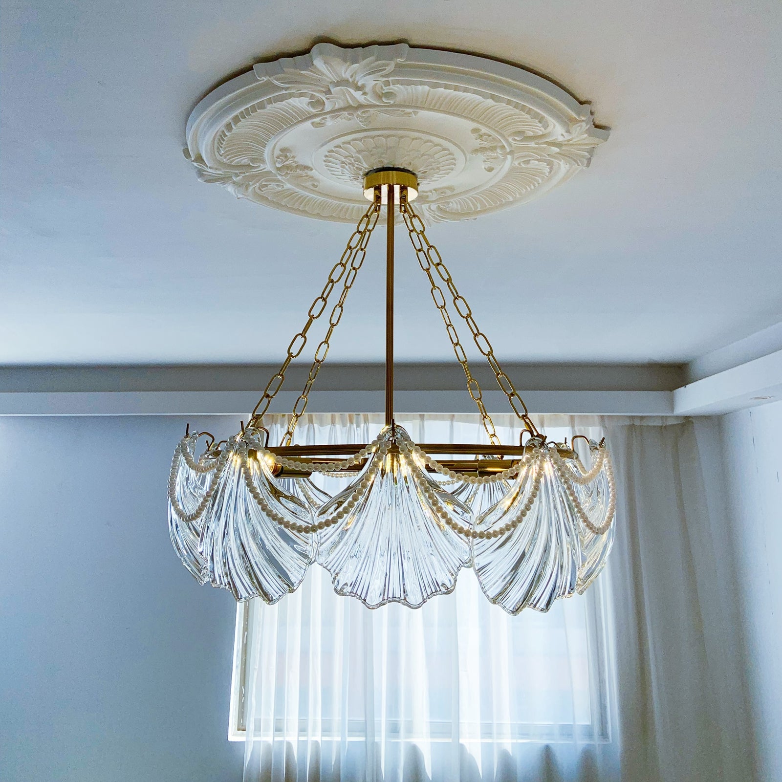 Decorative chandelier with clear glass and gold chains hanging from a ornate ceiling medallion.