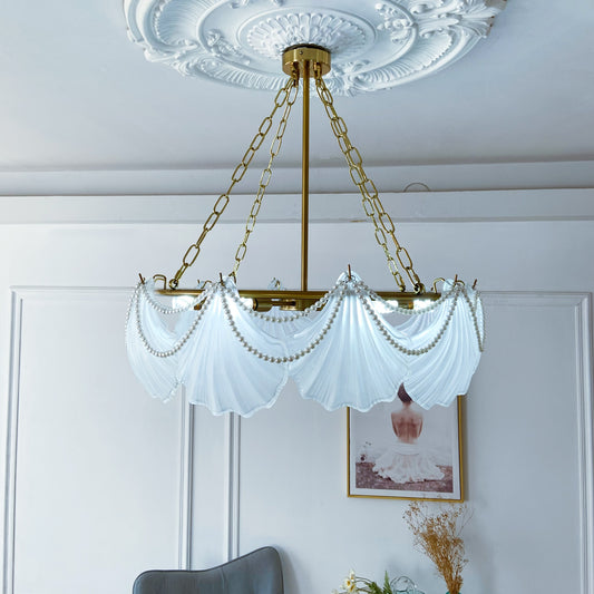Chandelier with glass and gold chain in a room with a white wall and framed picture.