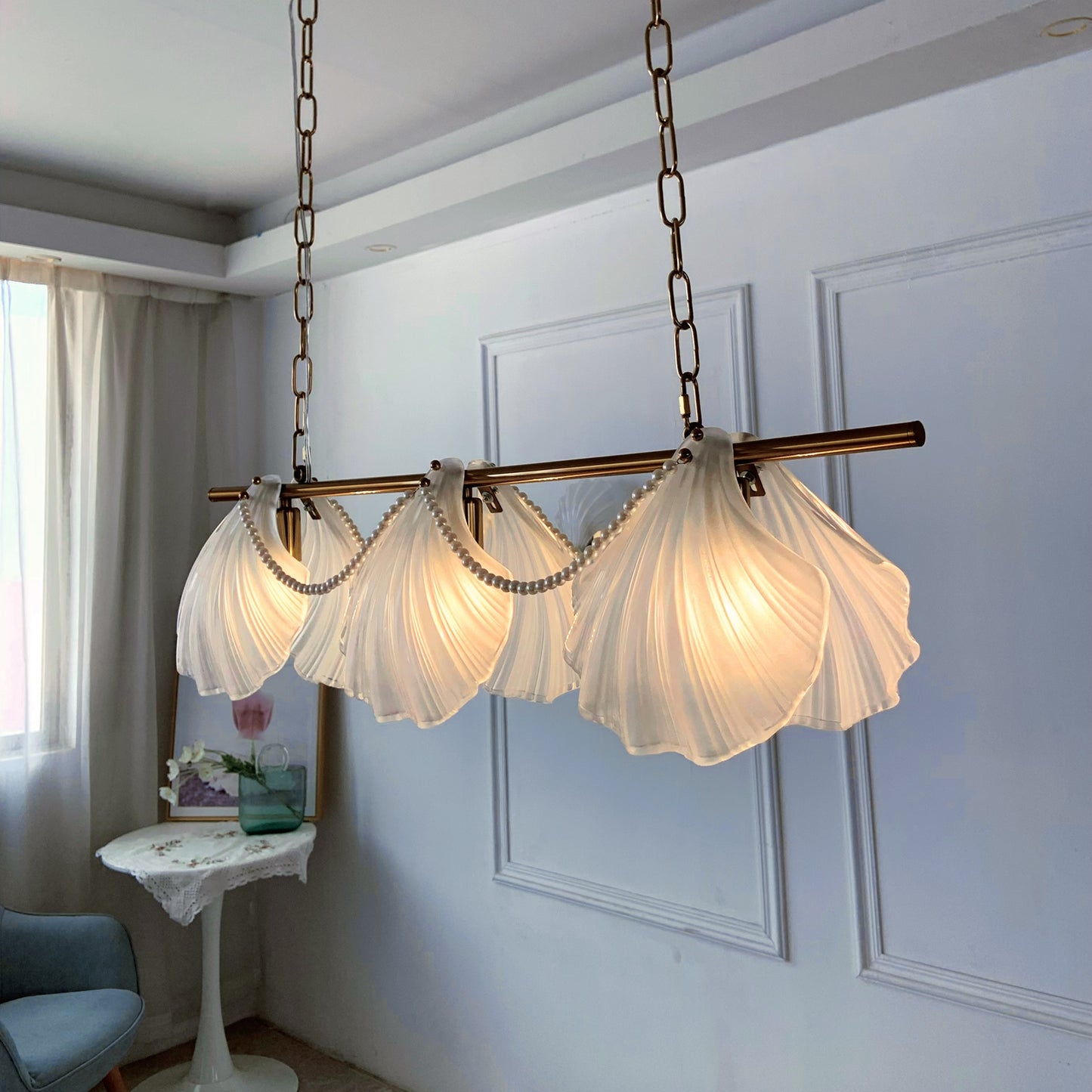 Chandelier with scalloped glass shades in a room with a window and chair.