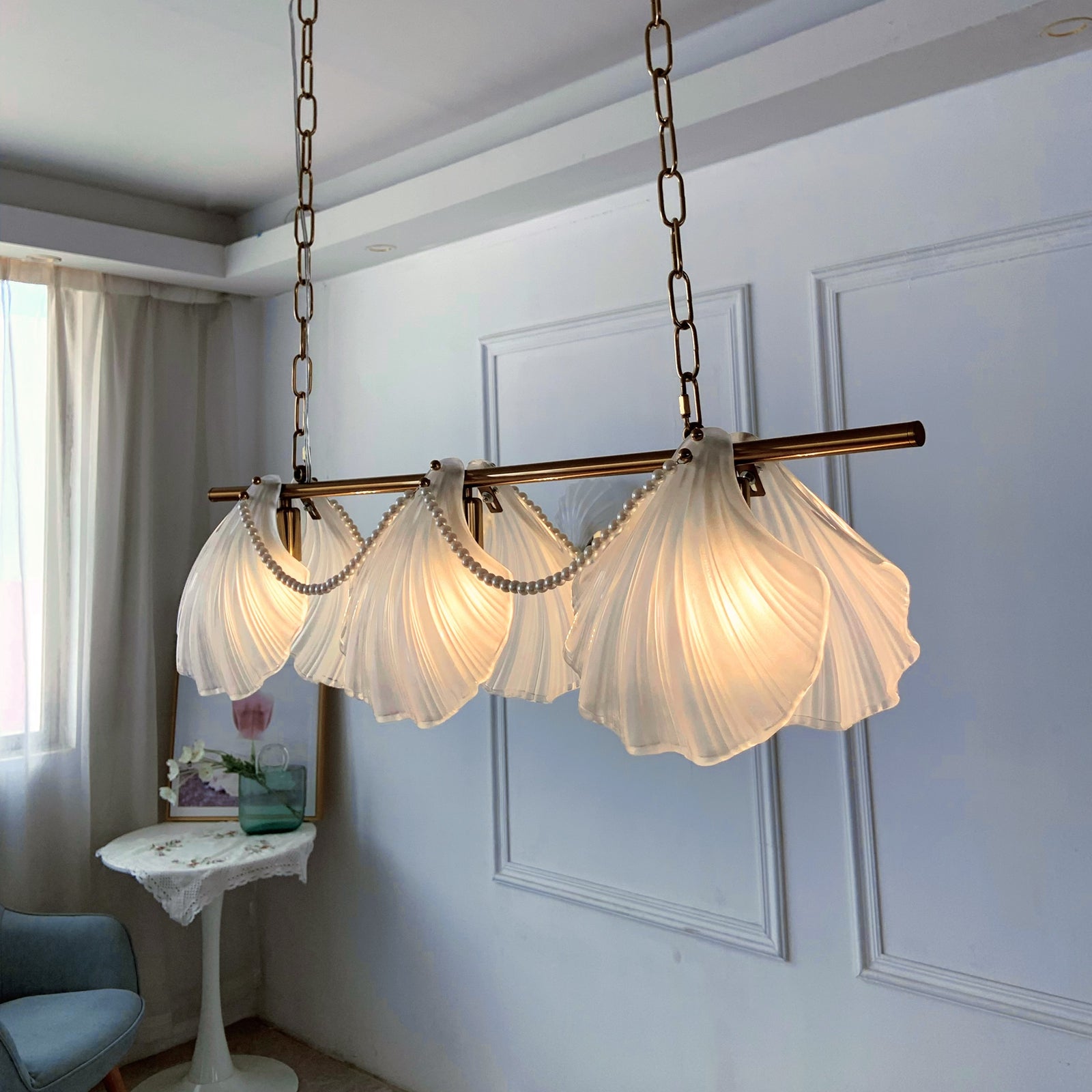 Chandelier with scalloped glass shades in a room with a window and chair.