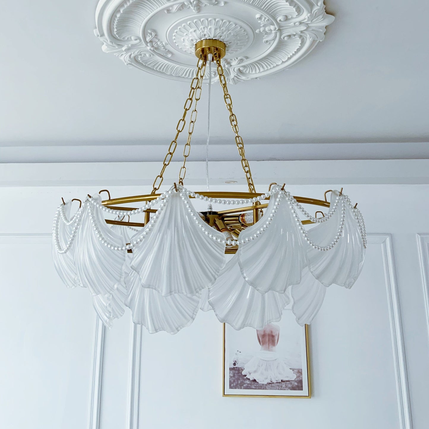 Glass Chandelier with white drapery and gold frame hanging in a room with decorative ceiling