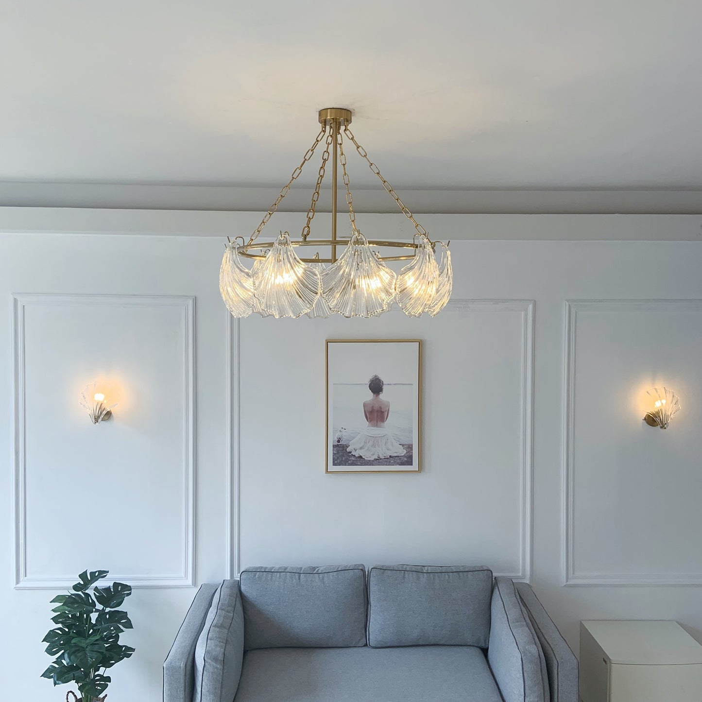 Chandelier hanging above a gray sofa in a living room with white walls and wall lights.