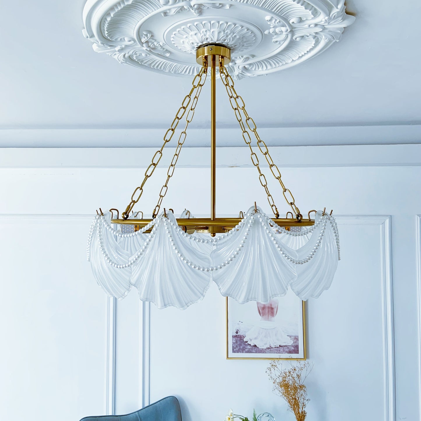 Decorative chandelier with white glass shades hanging in a room with light blue walls and a framed picture.