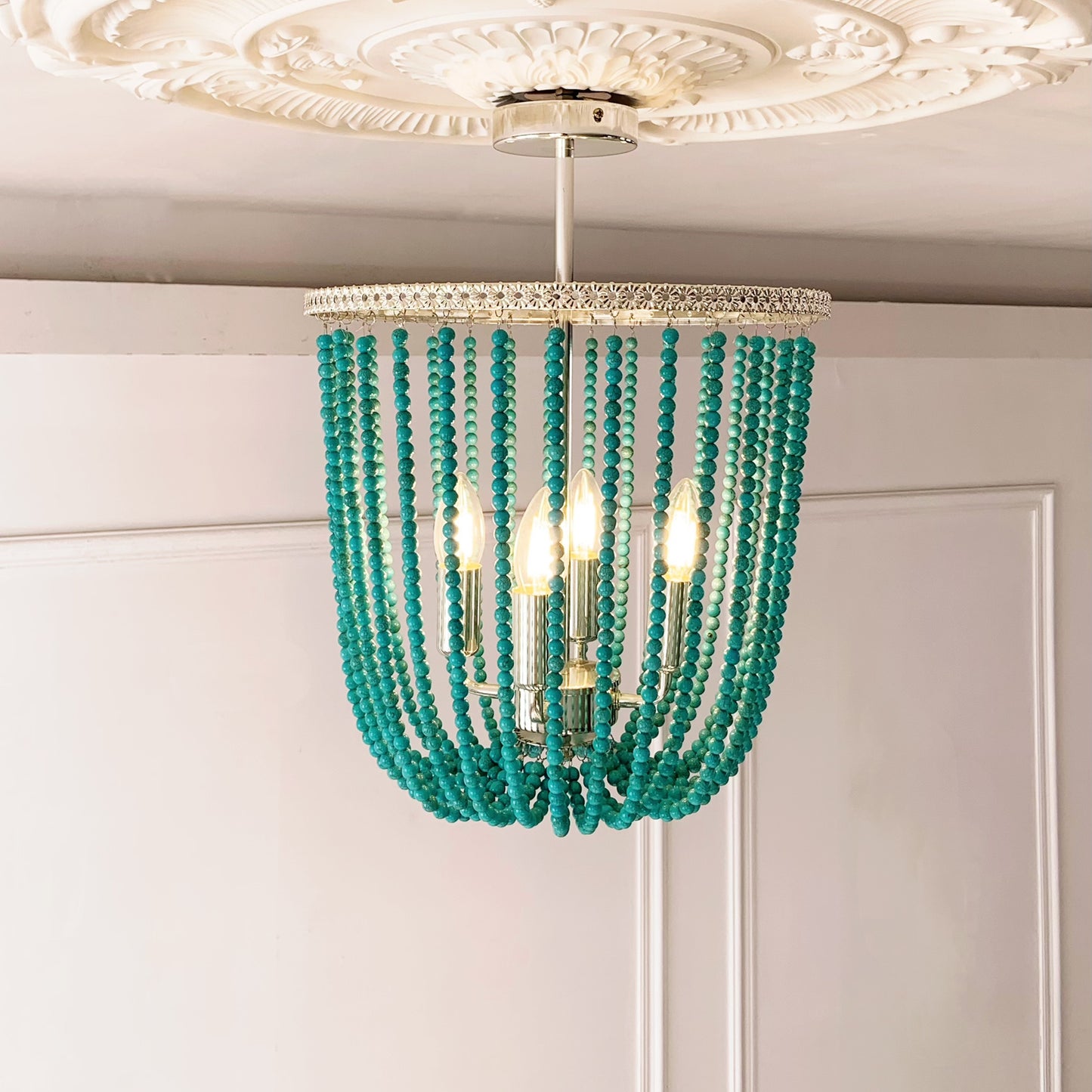 Turquoise beaded chandelier hanging from a decorative ceiling fixture.